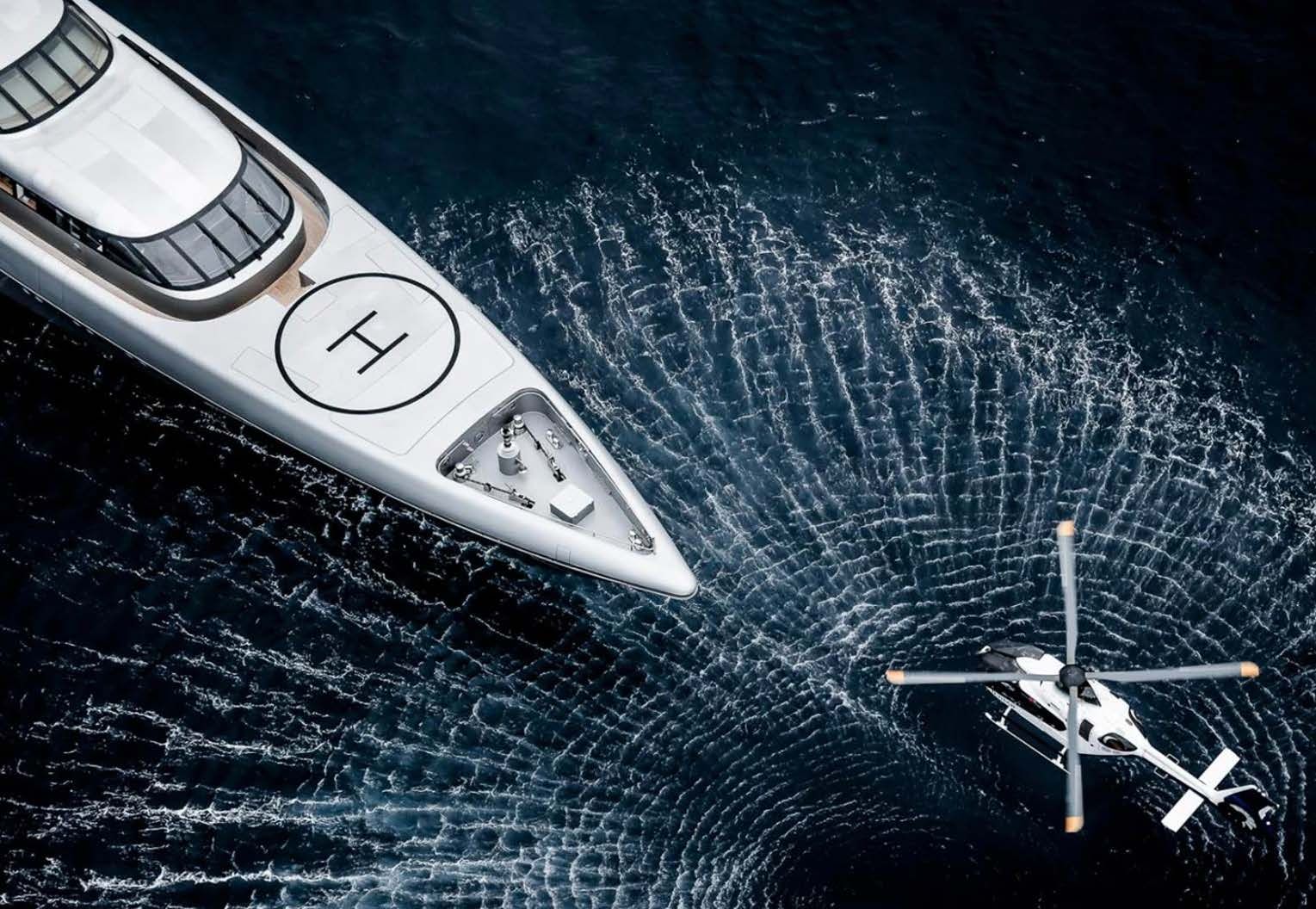 A superyacht at sea with a helicopter alongside, seen from above